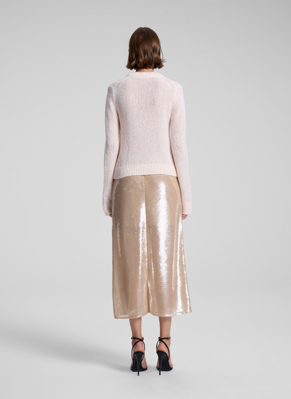 woman wearing light pink sweater and sequin midi skirt