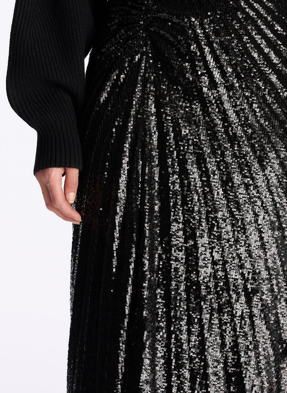 detail  view of a woman wearing a black cropped turtleneck sweater and black sequined pleated midi skirt
