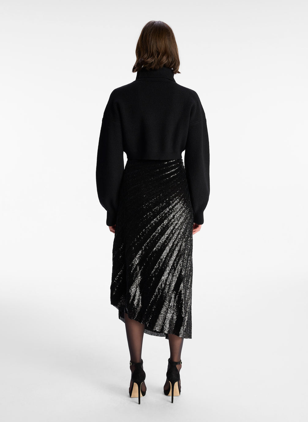 back view of woman wearing black long sleeve turtleneck wool sweater in cropped length with small split in the front hemline 