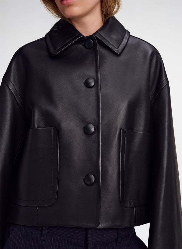 A close-up of a model wearing a black leather jacket with a wide collar, three large front buttons, and two large front patch pockets.