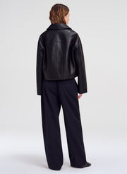 A model shown from the back wearing a black leather jacket and dark wide-leg trousers against a light gray studio background.