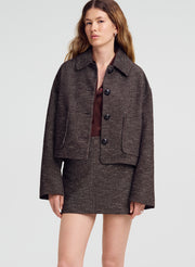 A woman modeling a dark brown tweed cropped jacket and matching mini skirt set against a light gray studio background.