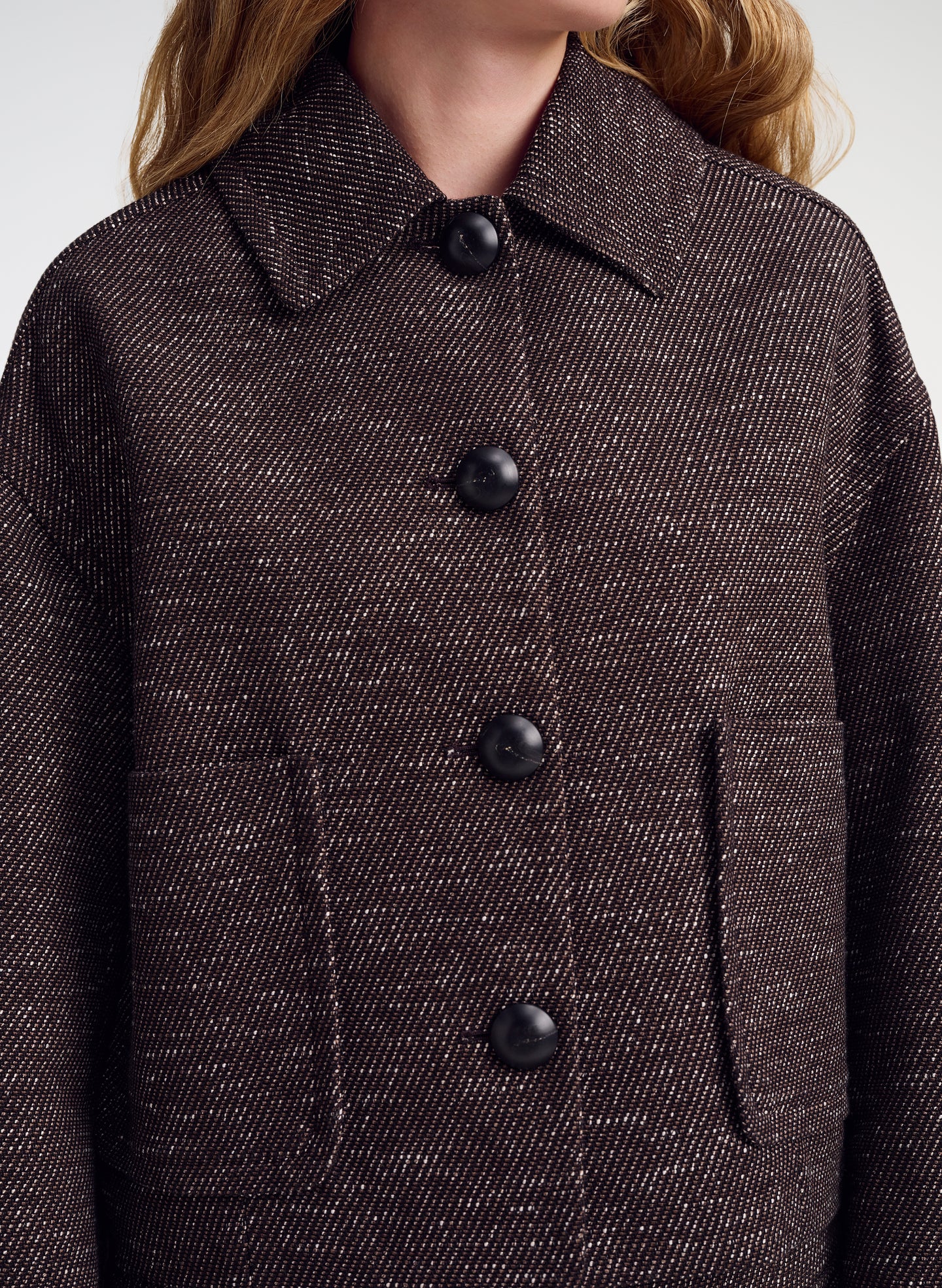 Close-up of a person wearing a dark brown textured tweed jacket with black buttons and a pointed collar.
