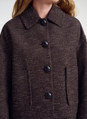 Close-up of a person wearing a dark brown textured tweed jacket with black buttons and a pointed collar.
