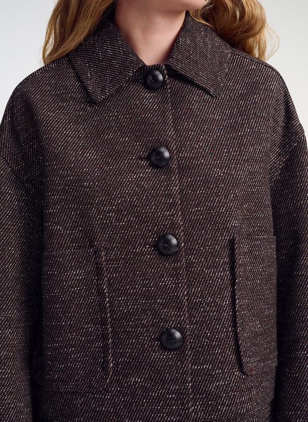 Close-up of a person wearing a dark brown textured tweed jacket with black buttons and a pointed collar.