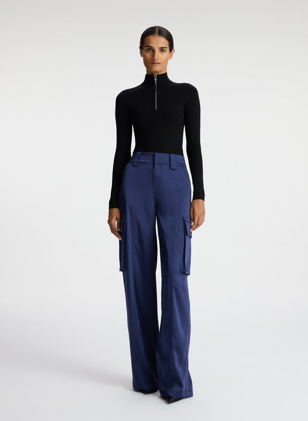 front view of woman wearing black knit long sleeve top and blue satin cargo pants