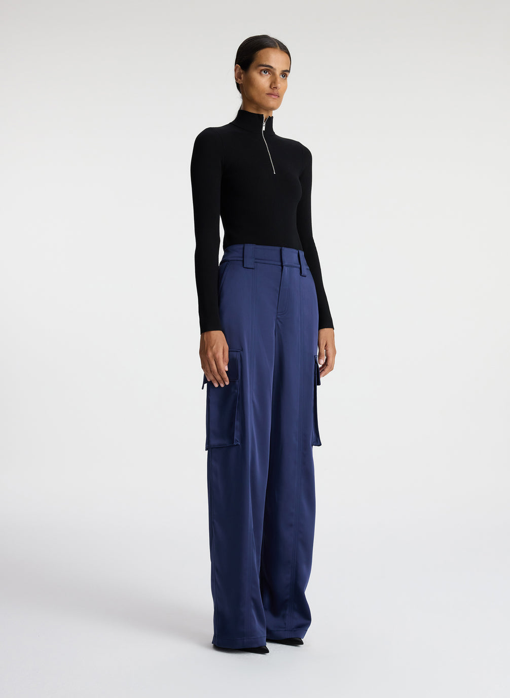 side view of woman wearing black knit long sleeve top and blue satin cargo pants