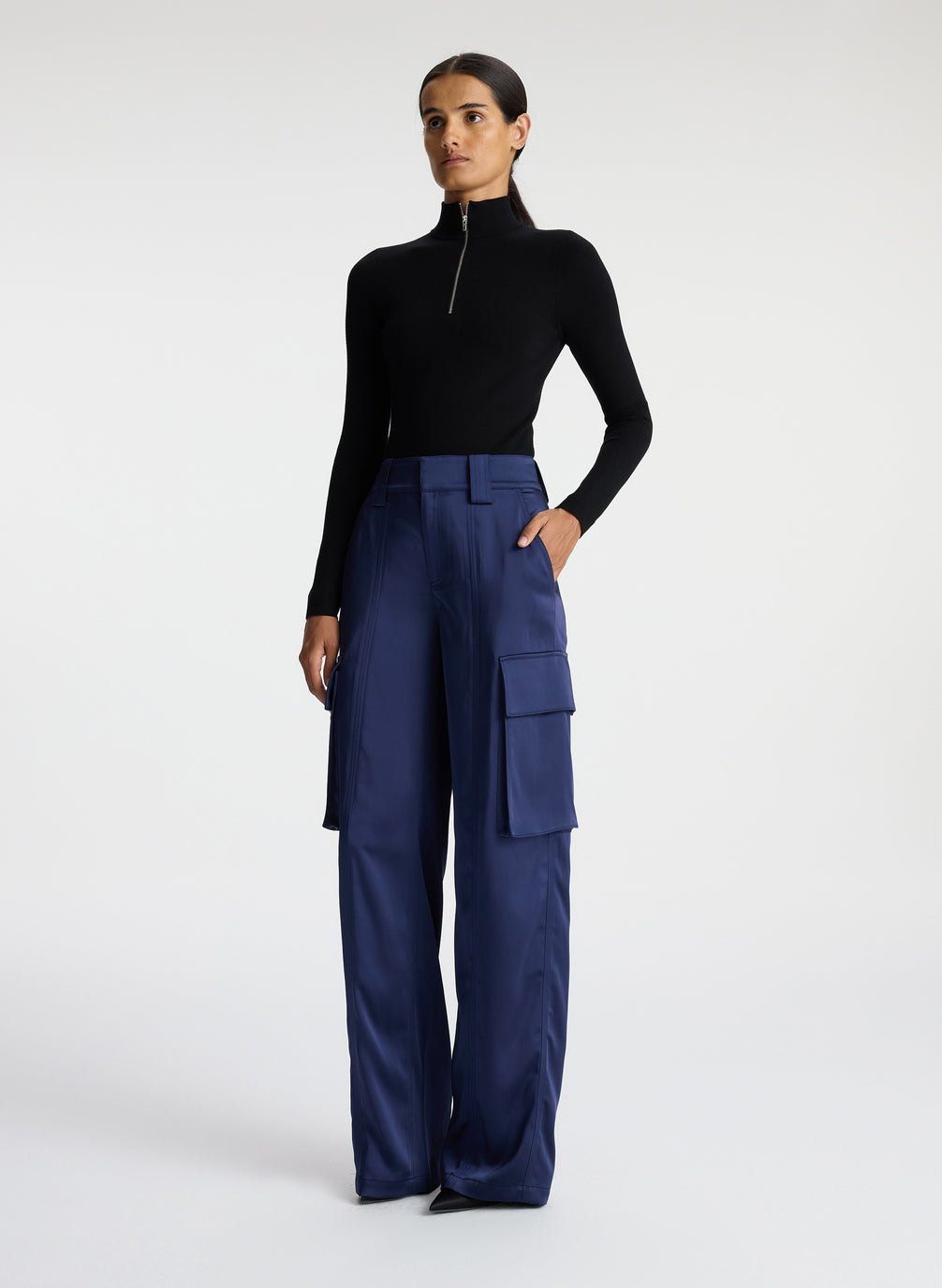 side view of woman wearing black knit long sleeve top and blue satin cargo pants