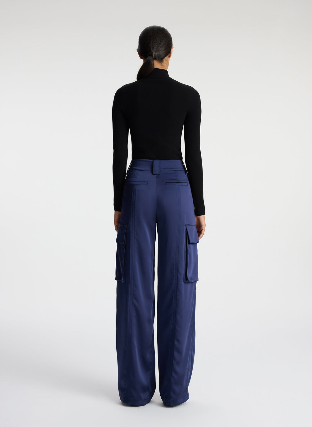 back view of woman wearing black knit long sleeve top and blue satin cargo pants
