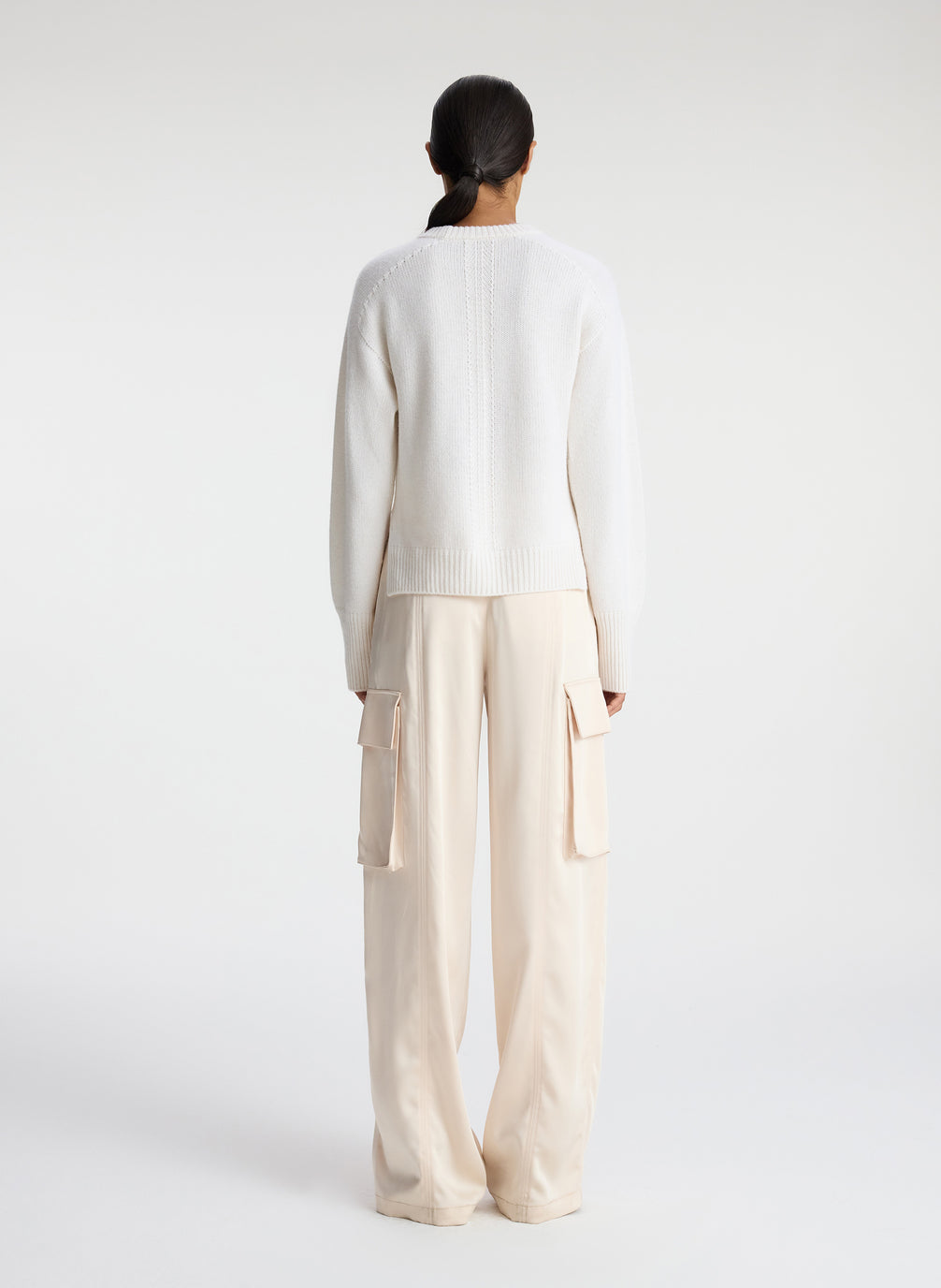 back view of woman wearing white sweater and beige satin cargo pants