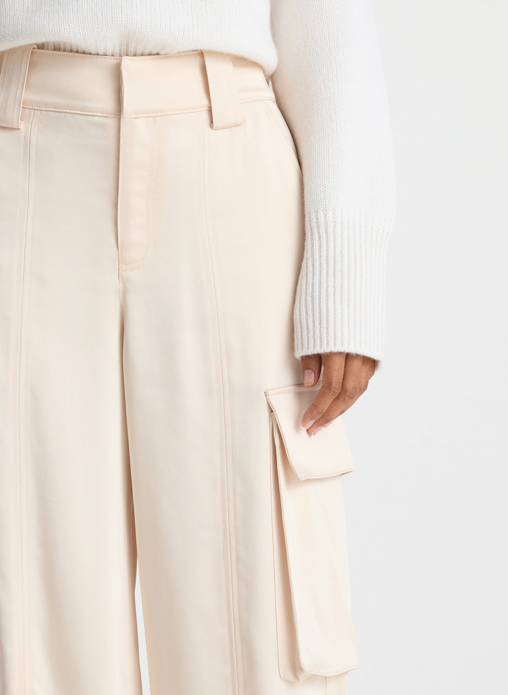 detail view of woman wearing white sweater and beige satin cargo pants