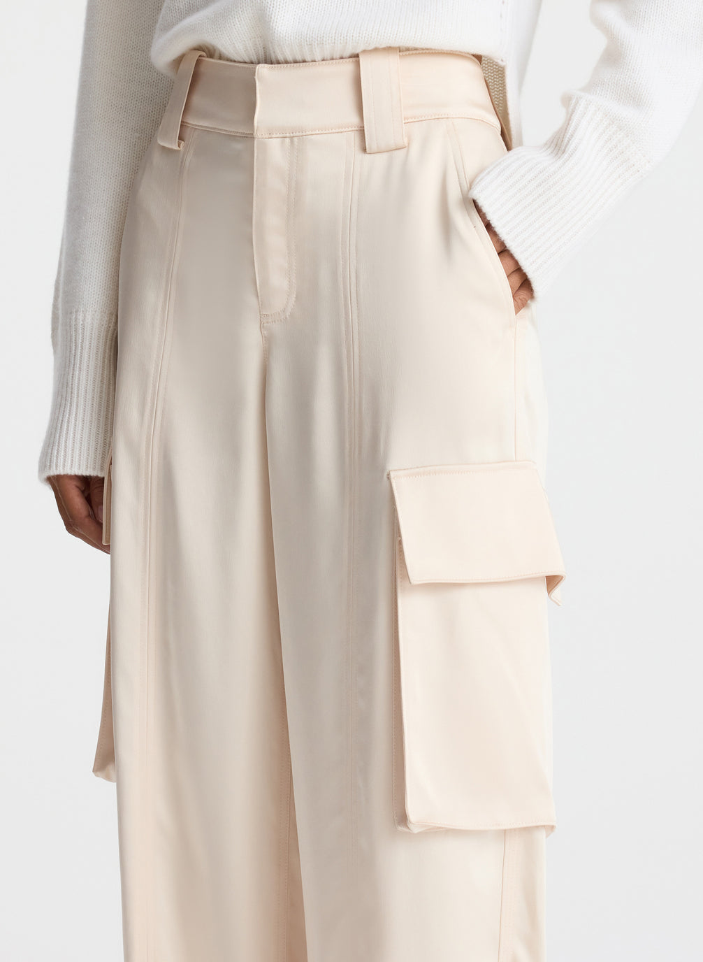 detail view of woman wearing white sweater and beige satin cargo pants