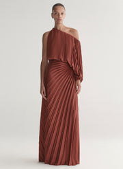 Woman wearing a one-shoulder rust-colored top with matching skirt with pleated details on a white background