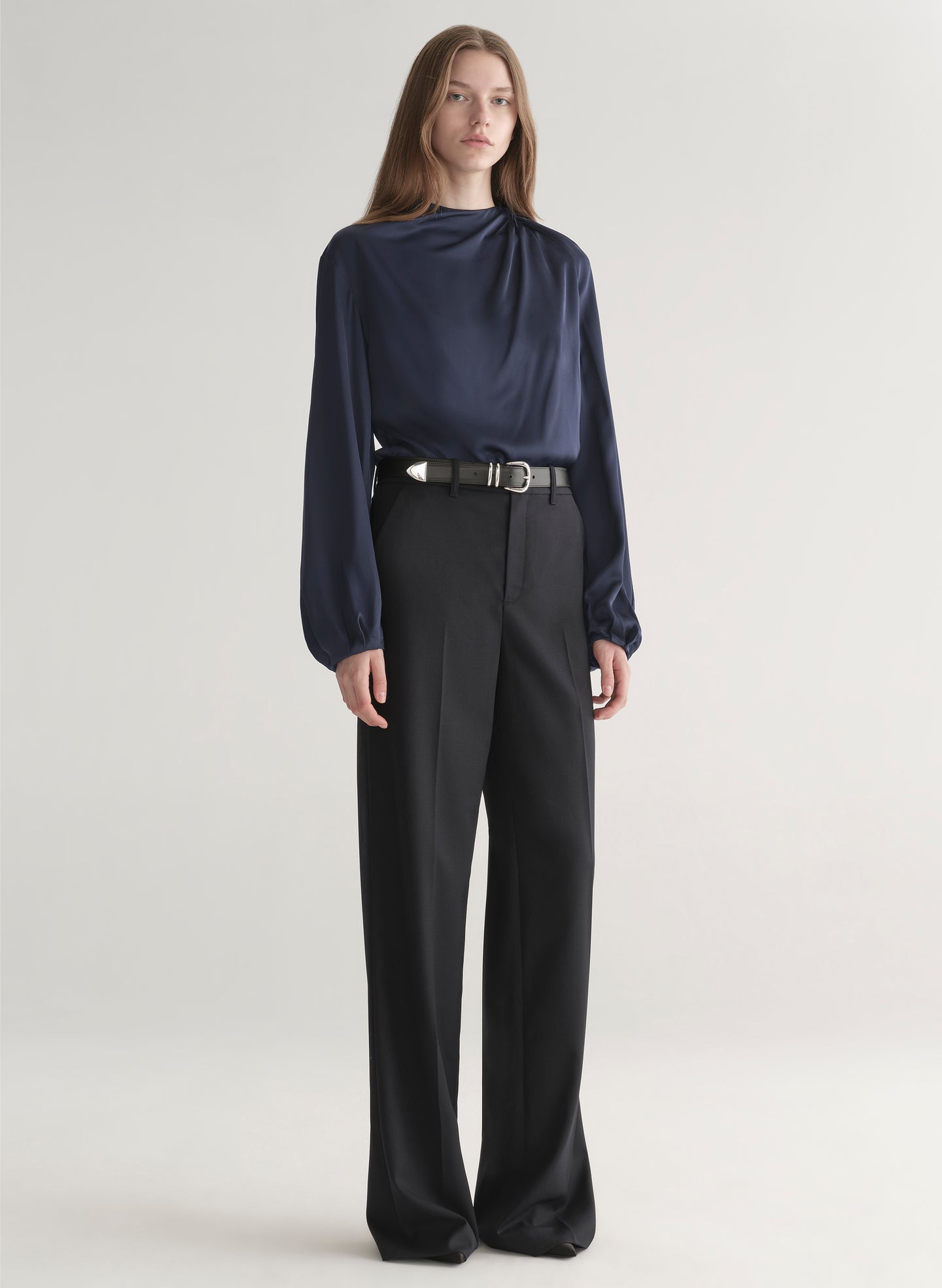 Woman wearing a navy blue blouse and black pants on a plain background