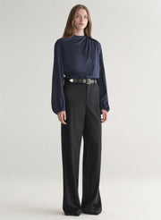 Woman wearing a navy blue blouse and black pants on a plain background