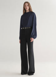 Woman wearing a navy blue blouse and black pants on a plain background