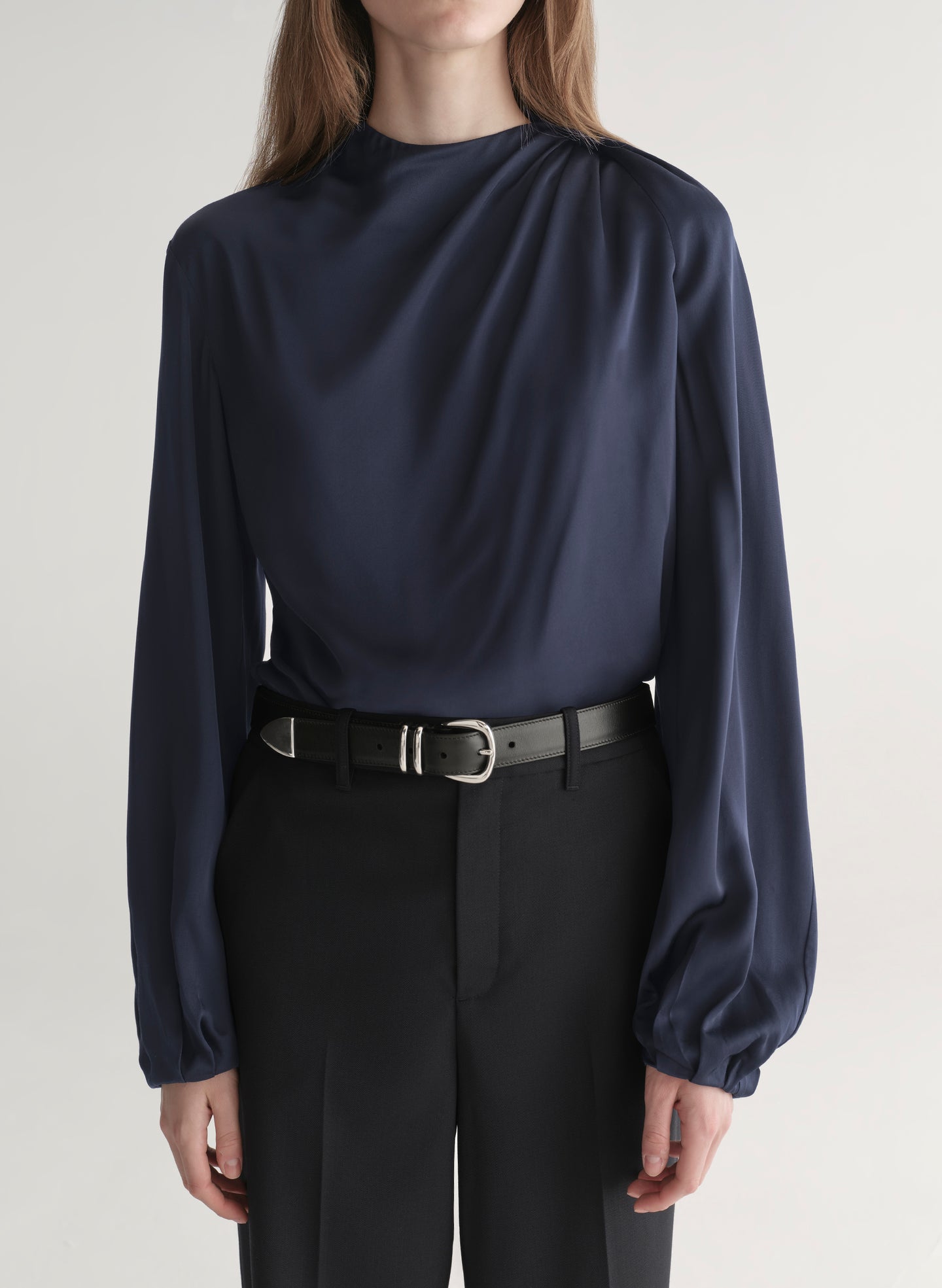 Woman wearing a navy blue blouse and black pants on a plain background