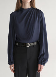 Woman wearing a navy blue blouse and black pants on a plain background