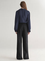 Woman wearing a navy blue blouse and black pants on a plain background