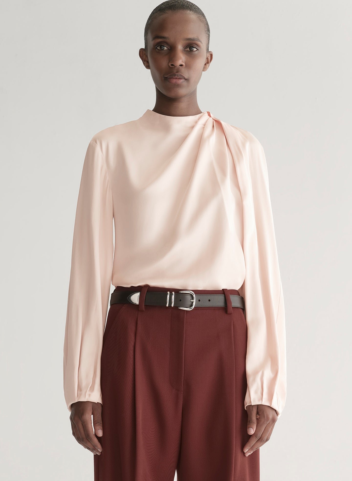 Person wearing a light pink blouse and maroon pants on a plain background