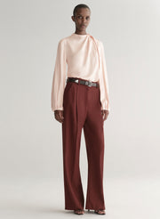 Person wearing a light pink blouse and maroon pants on a plain background