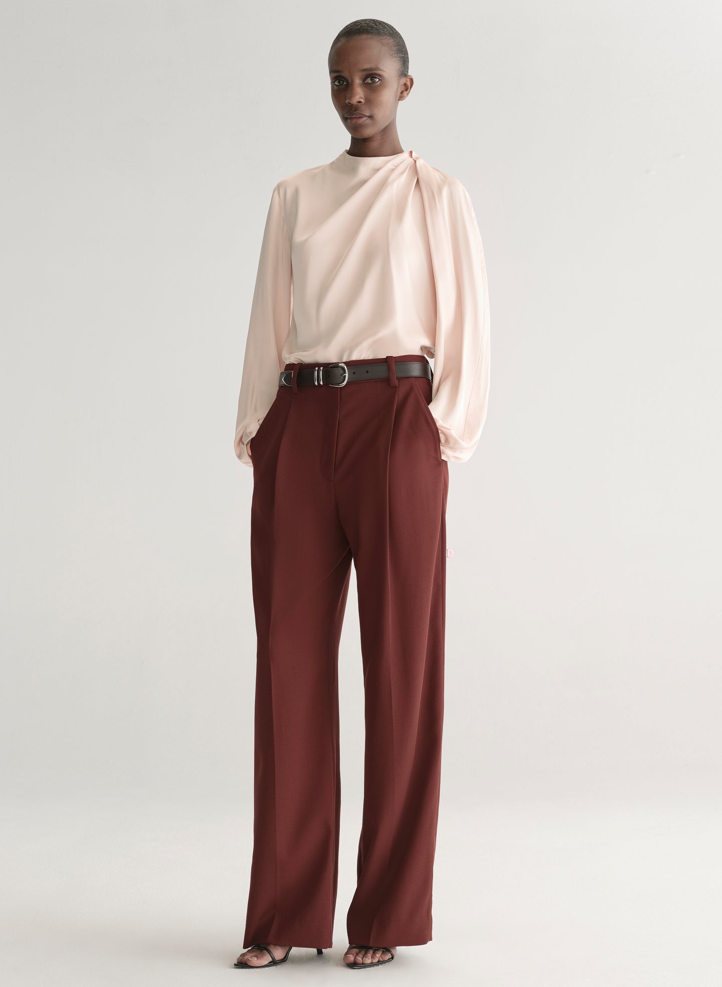 Person wearing a light pink blouse and maroon pants on a plain background