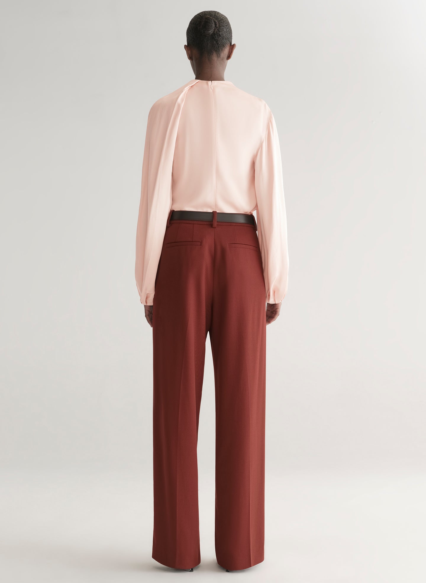Person wearing a light pink blouse and maroon pants on a plain background
