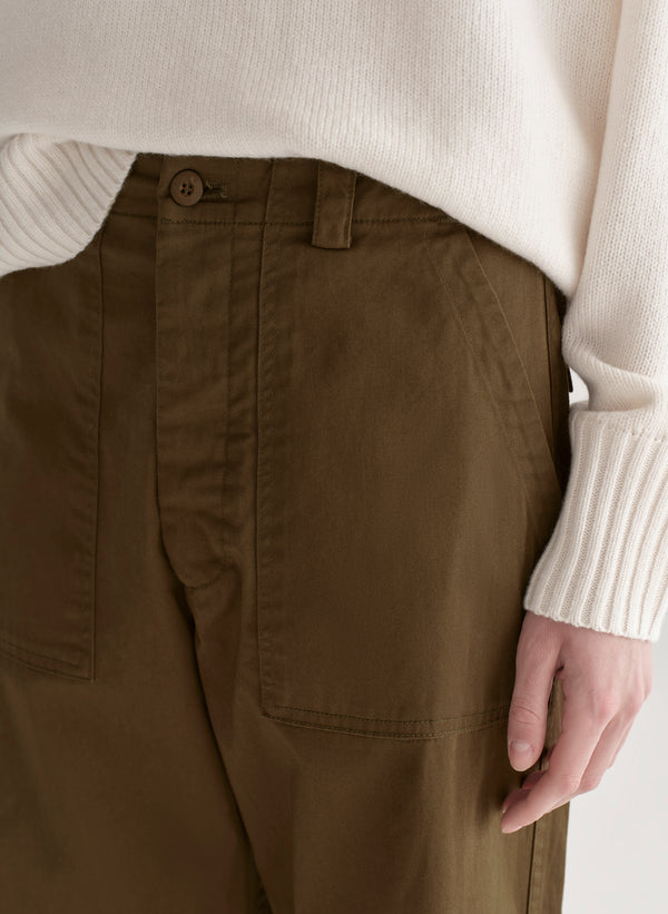 Woman wearing a white sweater and olive green pants on a plain background