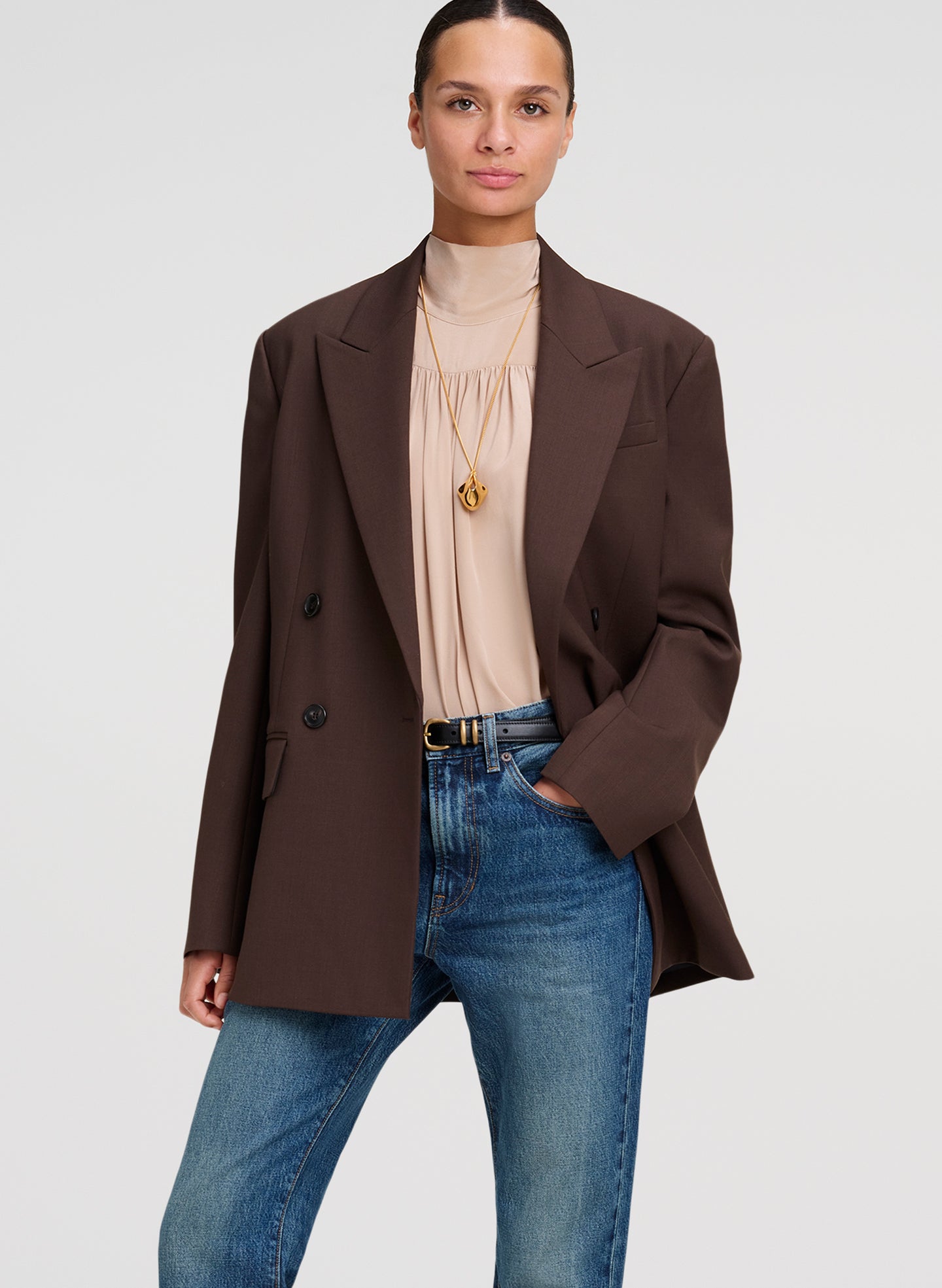 woman wearing brown blazer, beige silk top, and blue denim jeans