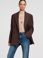 woman wearing brown blazer, beige silk top, and blue denim jeans