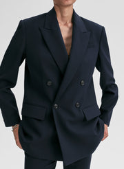 Person wearing a navy blue double-breasted blazer on a light gray background