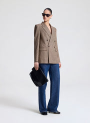 Person wearing a brown checkered blazer and blue jeans holding a black handbag on a white background