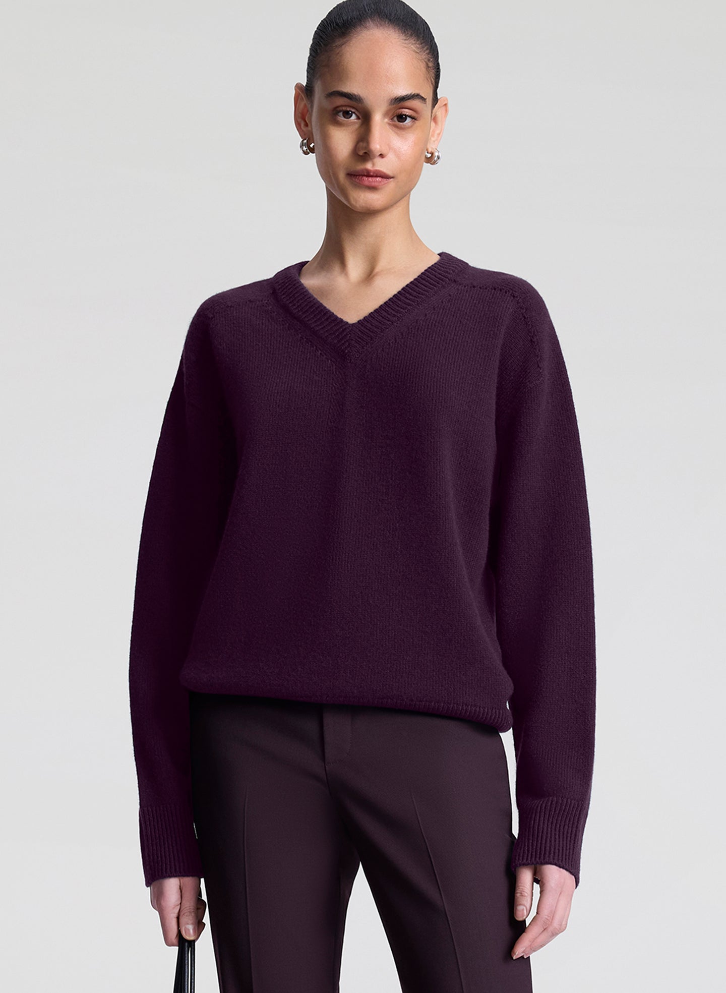 Person wearing a dark purple sweater and pants on a light gray background