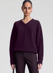 Person wearing a dark purple sweater and pants on a light gray background