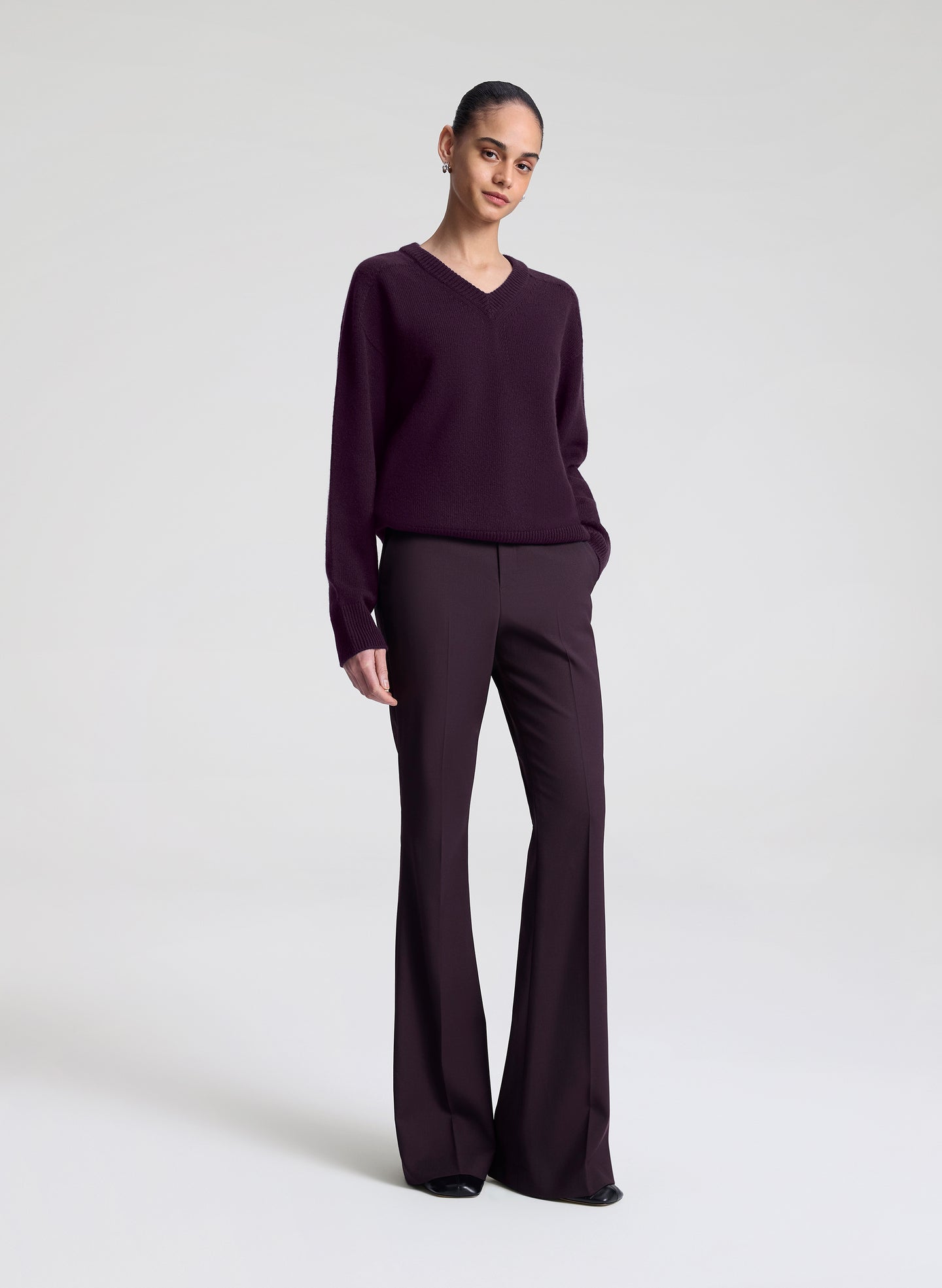 Person wearing a dark purple sweater and matching flared pants on a white background