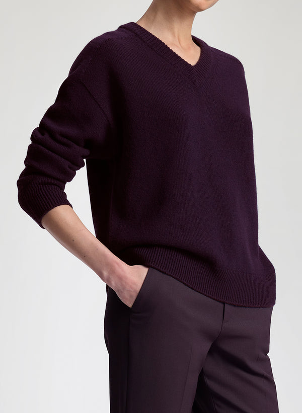 Person wearing a dark purple sweater and pants on a light gray background
