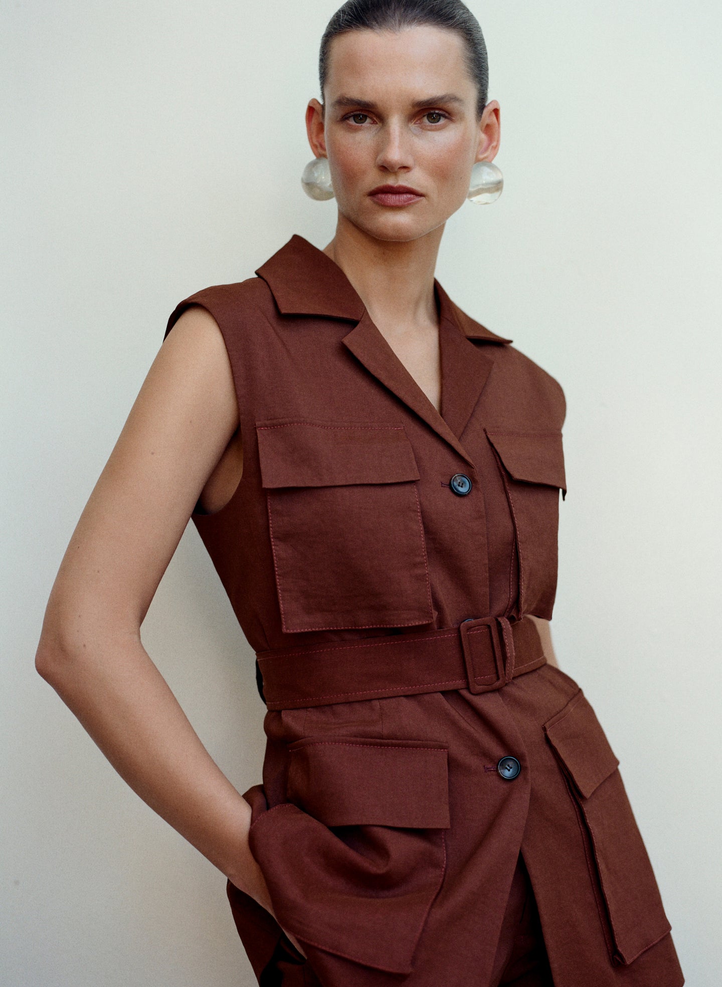 Woman wearing a brown sleeveless jacket and pants against a plain background