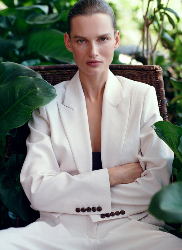 Woman in a white suit sitting in a chair surrounded by green plants