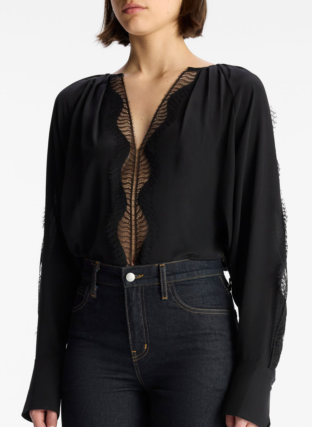 detail view of woman wearing black silk and lace long sleeve top and dark wash denim