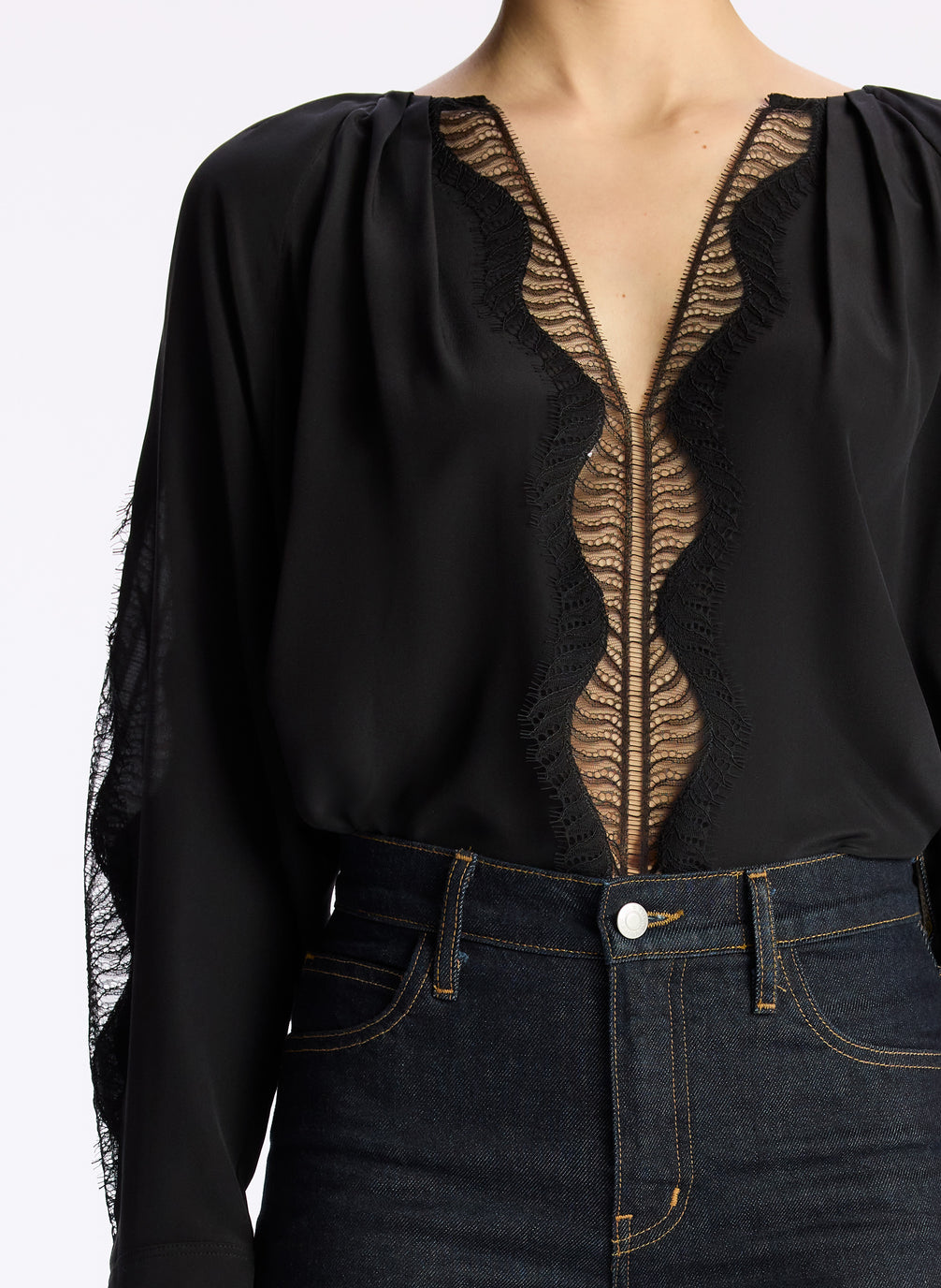 detail view of woman wearing black silk and lace long sleeve top and dark wash denim