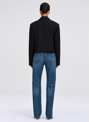 A model shown from the back wearing a black cropped blazer and blue jeans against a light gray studio background.