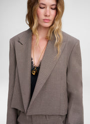 A woman wearing a cropped, structured blazer in a fine brown and beige houndstooth pattern, styled with a black top and a gold necklace.