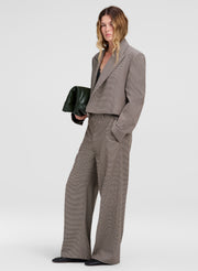 A model wearing a matching taupe gray cropped blazer and wide-leg trousers suit, holding a dark green clutch against a light gray studio background.