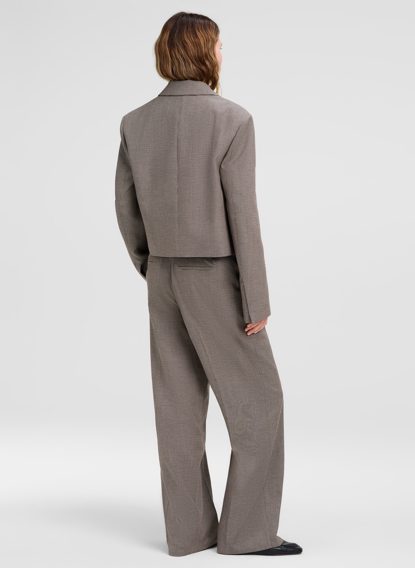 A model shown from the back wearing a matching gray cropped blazer and wide-leg trousers set, photographed against a light gray studio background.