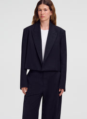 A model wearing a dark navy pinstripe cropped blazer and matching wide-leg trousers over a white top, shot against a light gray studio background.