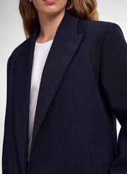 A close-up of a model wearing a dark navy blue pinstripe blazer over a white crewneck top, cropped from the lower face to the waist.