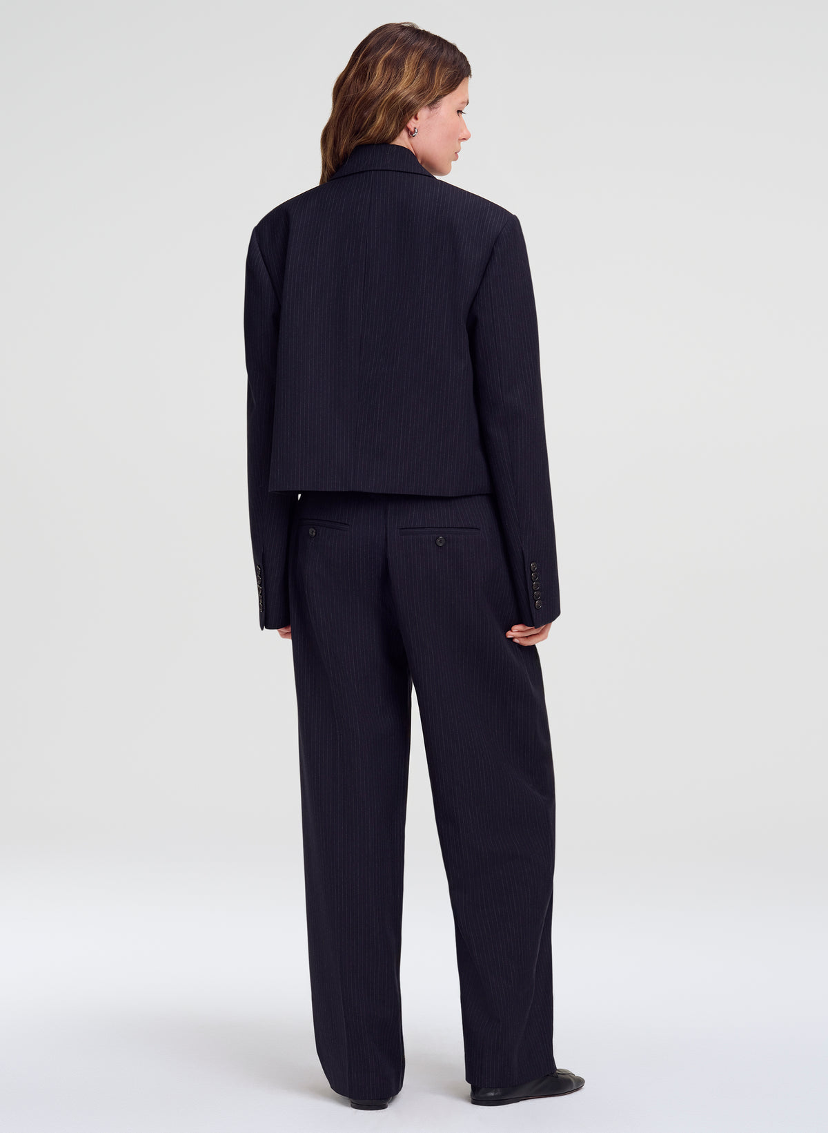A model shown from the back wearing a dark navy blue cropped blazer and matching wide-leg trousers against a light gray studio background.