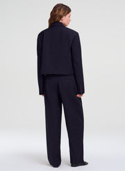 A model shown from the back wearing a dark navy blue cropped blazer and matching wide-leg trousers against a light gray studio background.