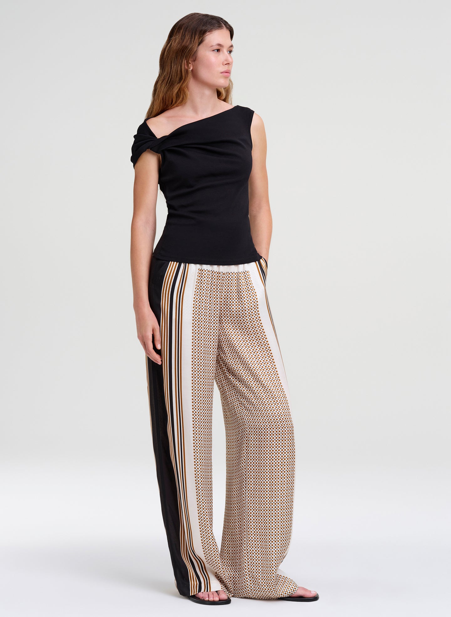 Woman wearing a black off-shoulder top and patterned pants on a white background