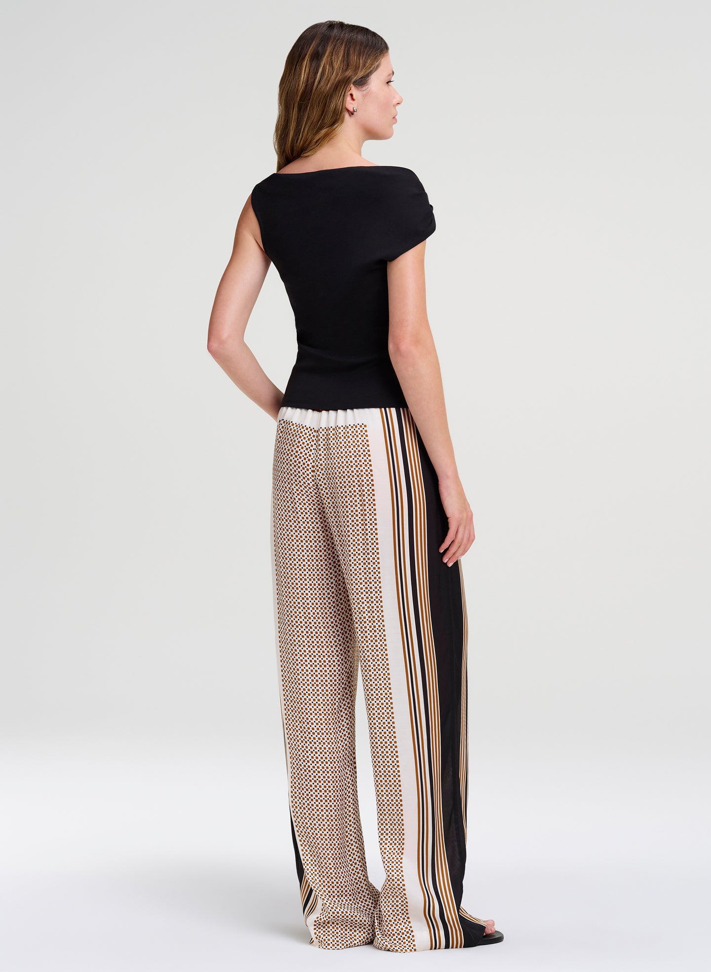 Woman wearing a black top and patterned pants with side stripes on a white background